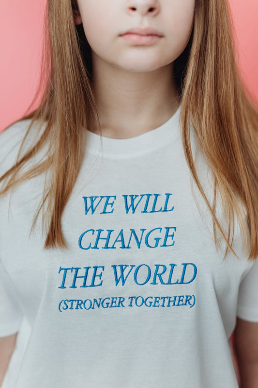 Affirmation tee with “We will change the world” embroidery on woman, pink backdrop